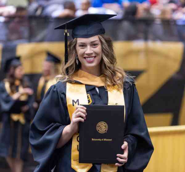 Chelsea Hoyer, MSW, wearing her graduation cap and gown and holding her diploma at her commencement ceremony.