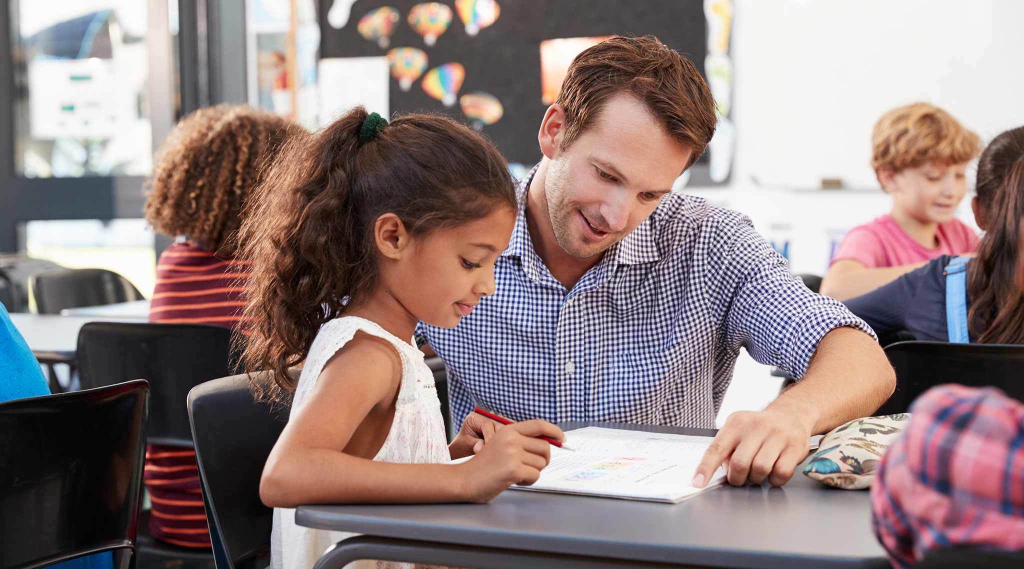 Teaching point to a notebook with a child at a desk in a classroom setting.