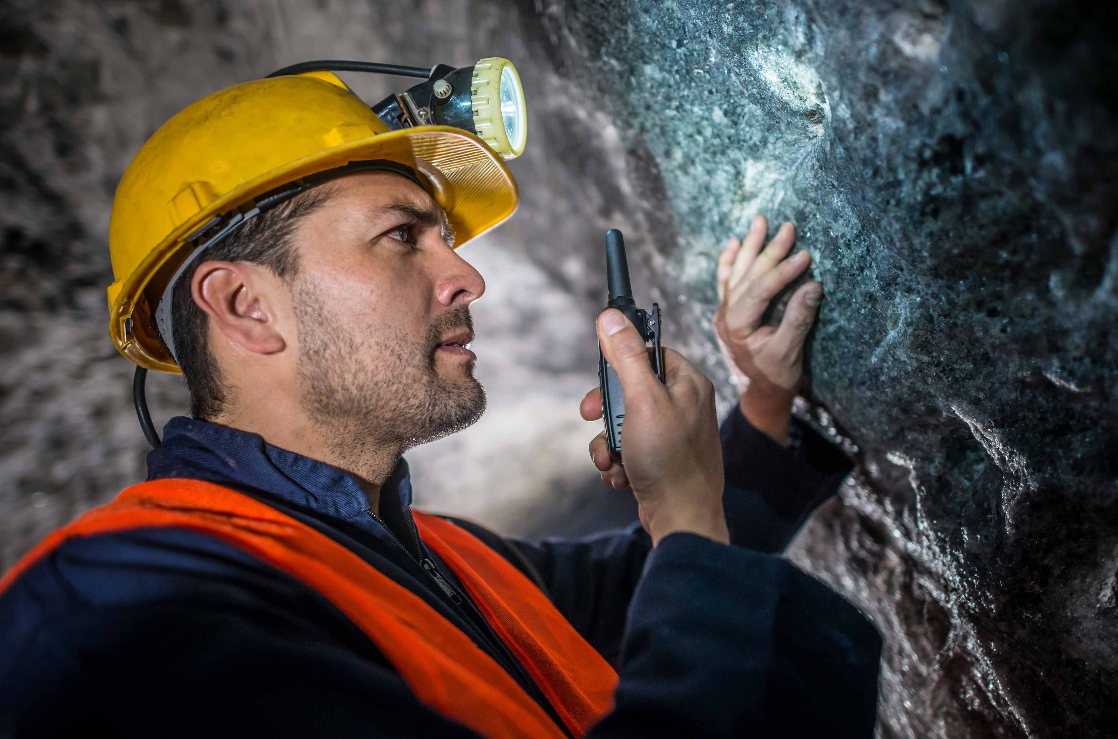 Mine worker inspecting mine with flashlight, wearing safety gear.