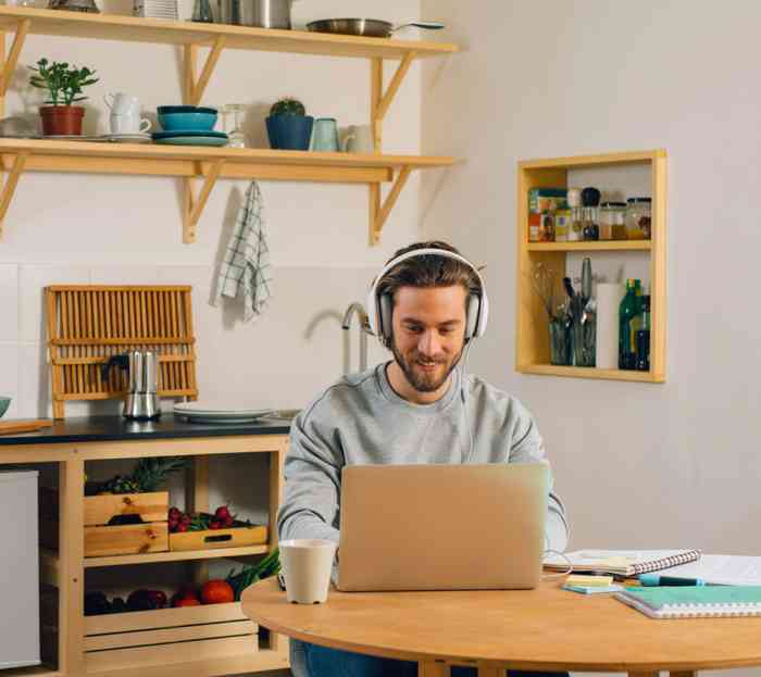 Young Caucasian man with headphones using his laptop at the kitchen table.