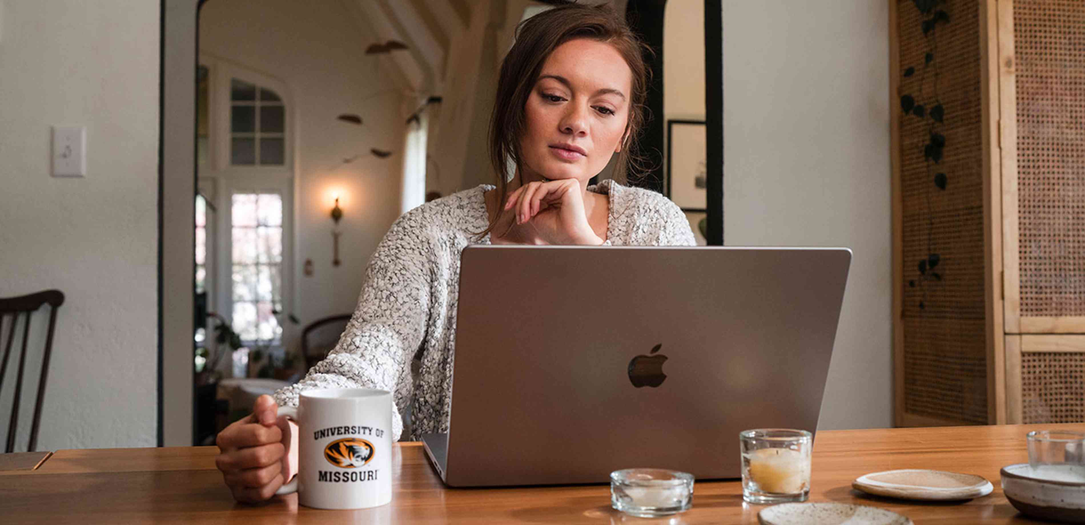 A woman on a laptop holding a Mizzou coffee mug.