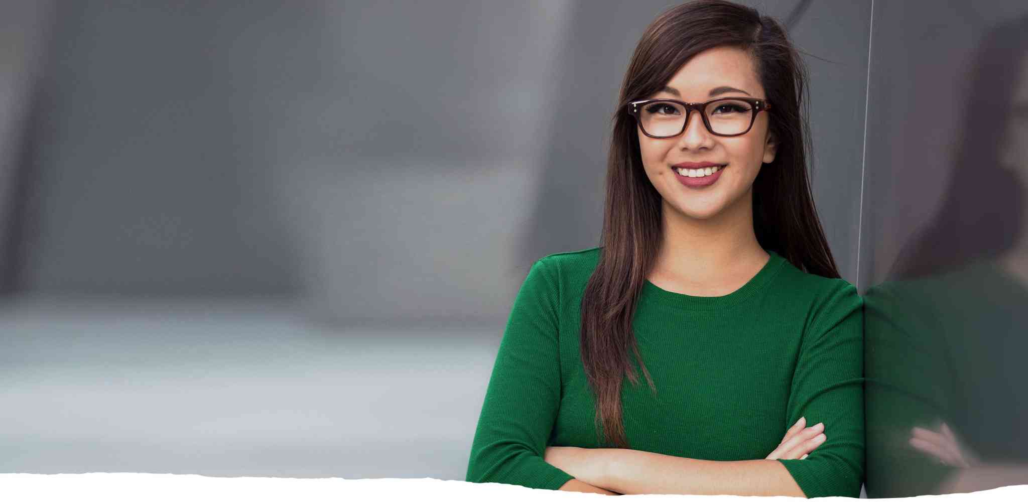 Woman in green shirt wearing glasses and crossing arms across body.
