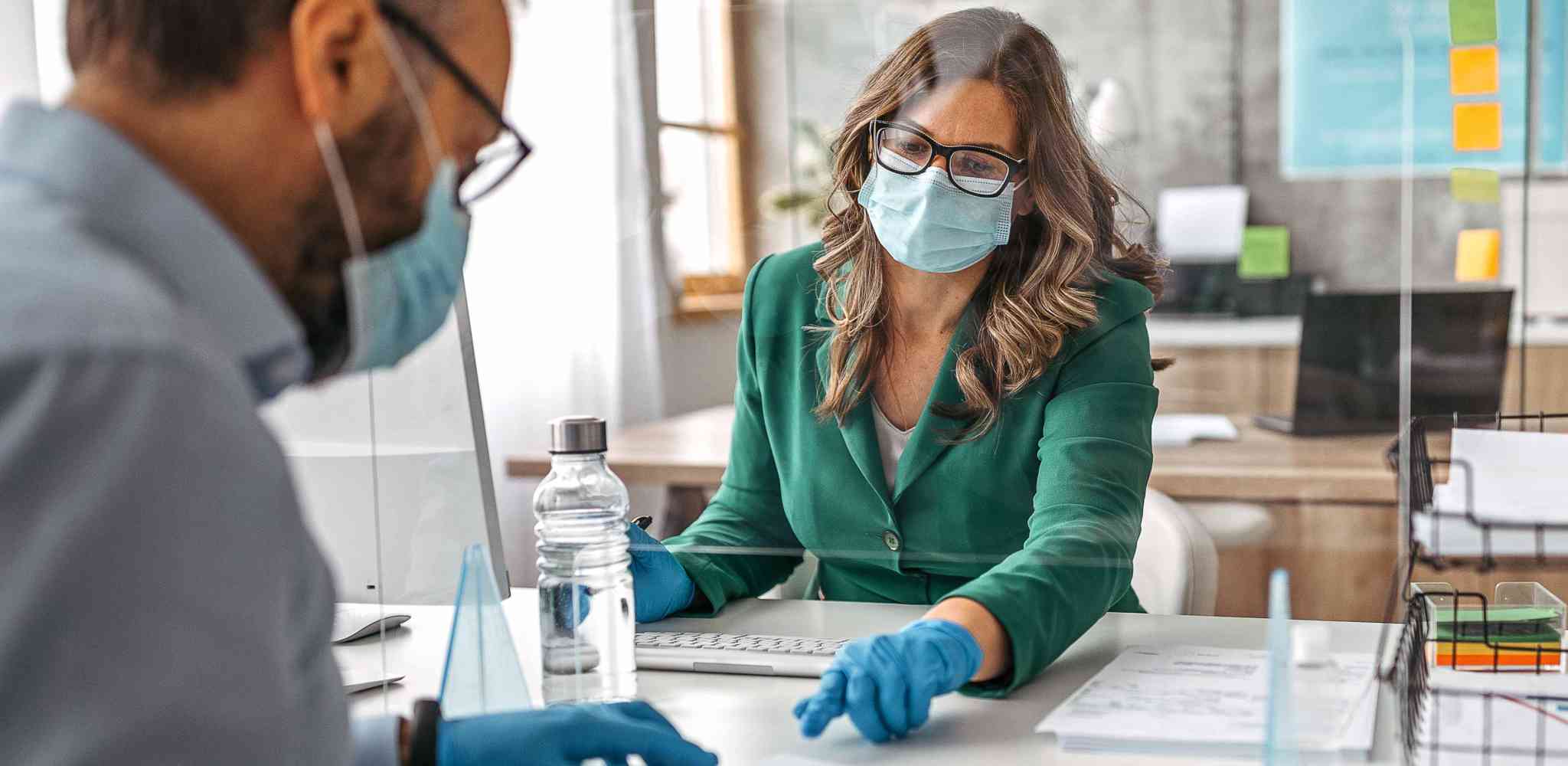 Public health professional wearing protective gloves and face mask. Office with acrylic glass partition on desk. Acrylic glass wall - protection against coughs and spitting, protection against viruses.