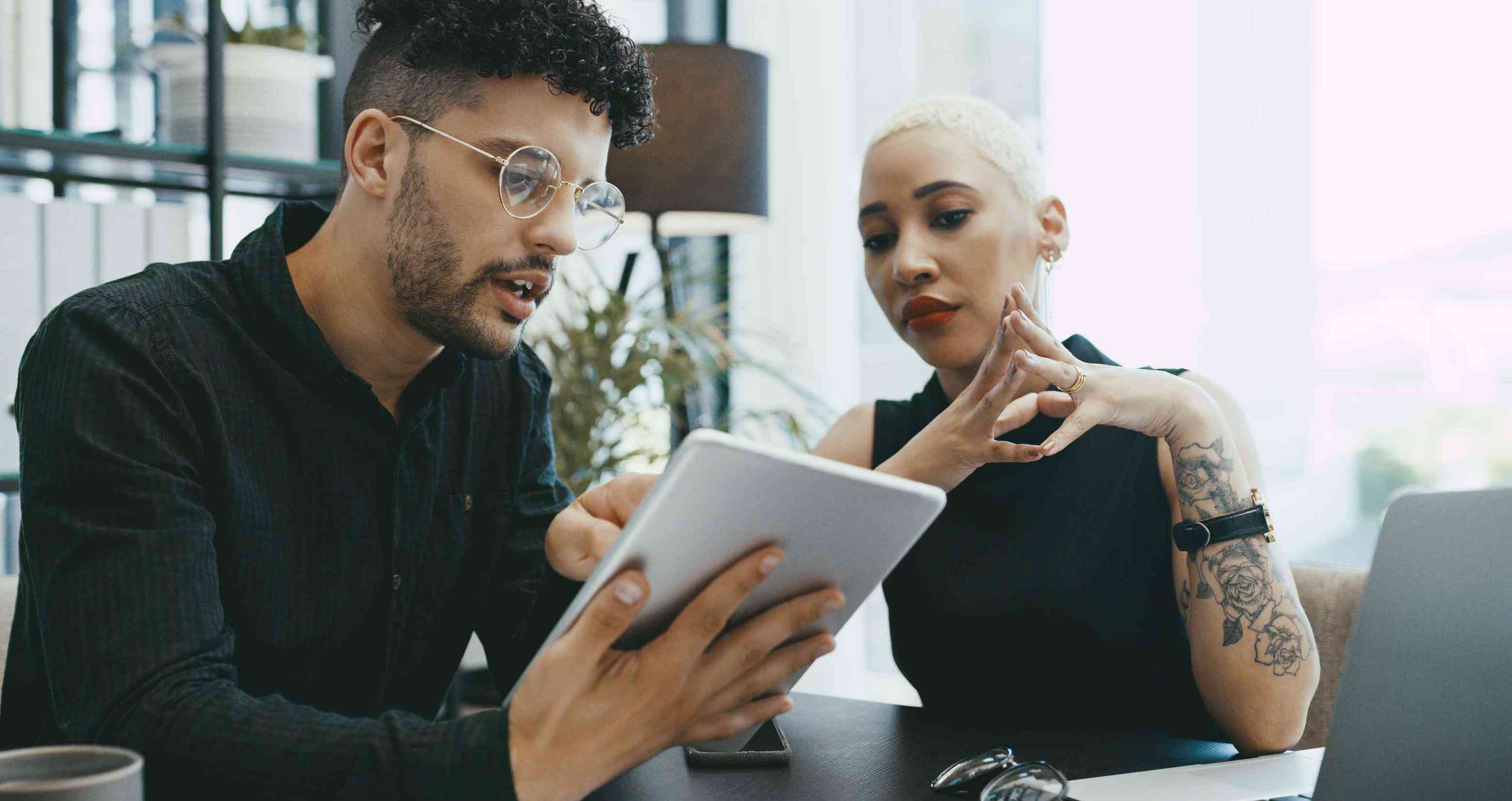 Two people sitting at an office table looking at a tablet.