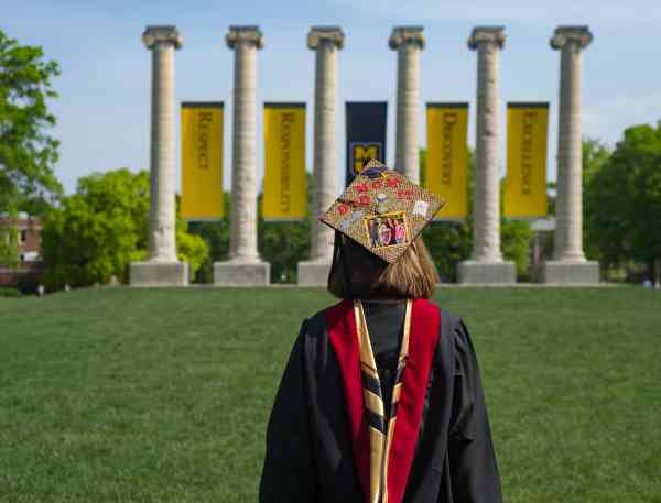 Mizzou graduate JoDee Kenney facing the columns on Mizzou's campus on graduation day; her graduation cap reads Mom Did It.