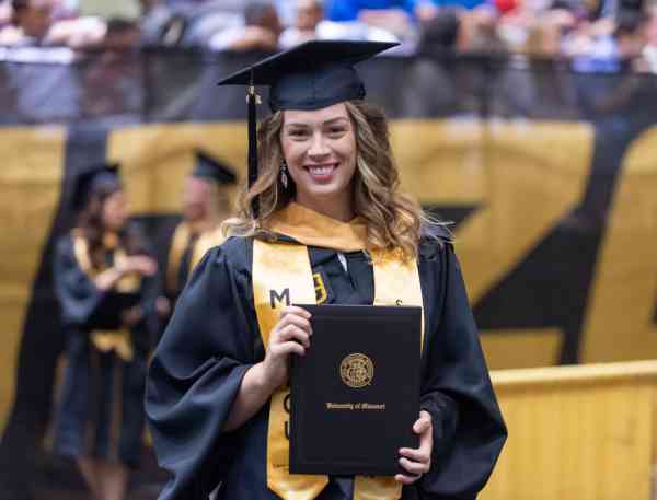 Chelsea Hoyer, MSW, wearing her graduation cap and gown and holding her diploma at her commencement ceremony.