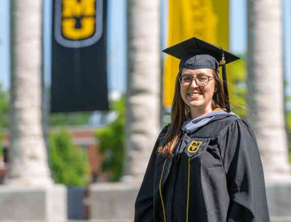 Stephanie Gillam, biomedical sciences MS, wearing a graduation cap and gown in front of Mizzou's columns.