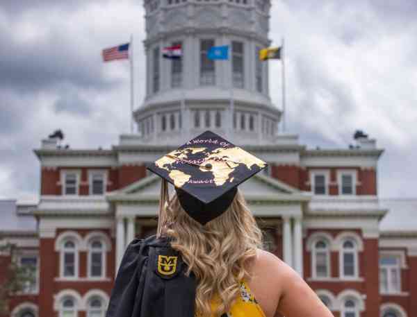 Sarah Swoboda, bachelor's in business administration, faces Jesse Hall on Mizzou's campus at commencement; her graduation cap reads A world of endless possibilities.