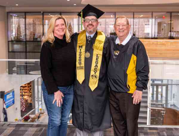 Neil Schmedding, BHS, wearing his graduation cap and gown, standing next to his sister and father, who are both Mizzou graduates.