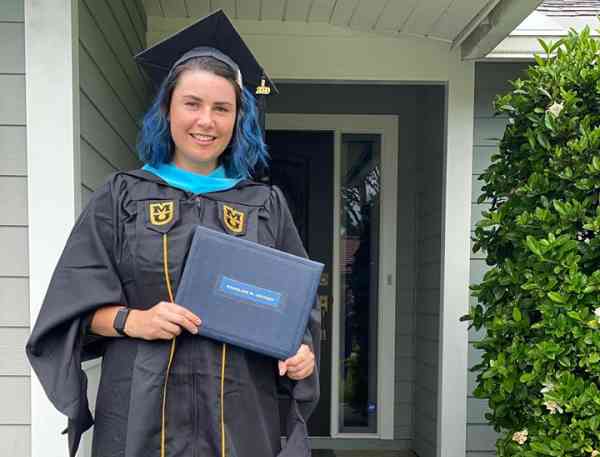 Maddie Jeffrey, positive coaching and athletic leadership, stands with her diploma in her graduation cap and gown; a sign in her yard reads Mizzou Made, class of 2020.
