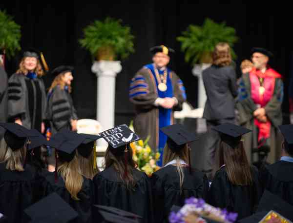 Graduating students at a commencement ceremony; focus on a graduation cap that reads Just Did It.