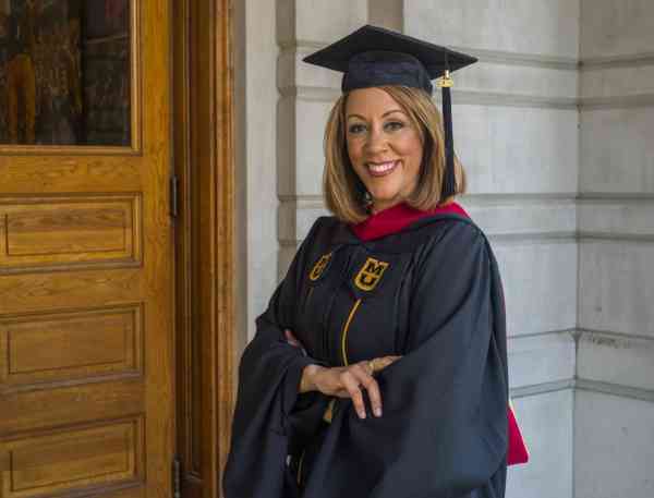 JoDee Kenney, MA in journalism, interactive media, wearing her graduation cap and gown.