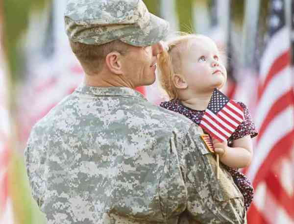 Military hero and child standing by American flags.
