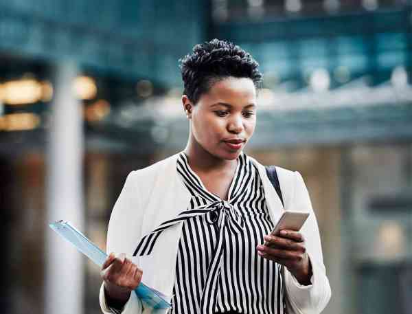 Professional carrying a clipboard and looking at a phone.
