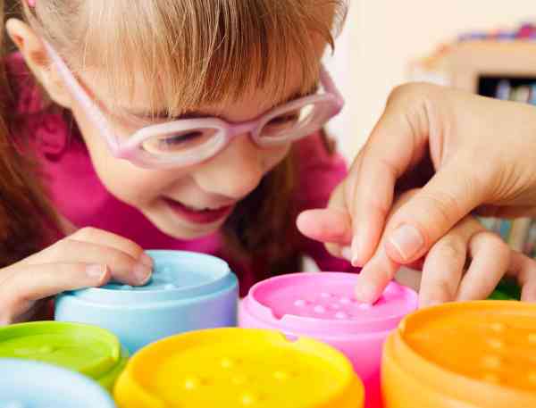 Hands of an occupational therapist helping a young child use some sensory toys.