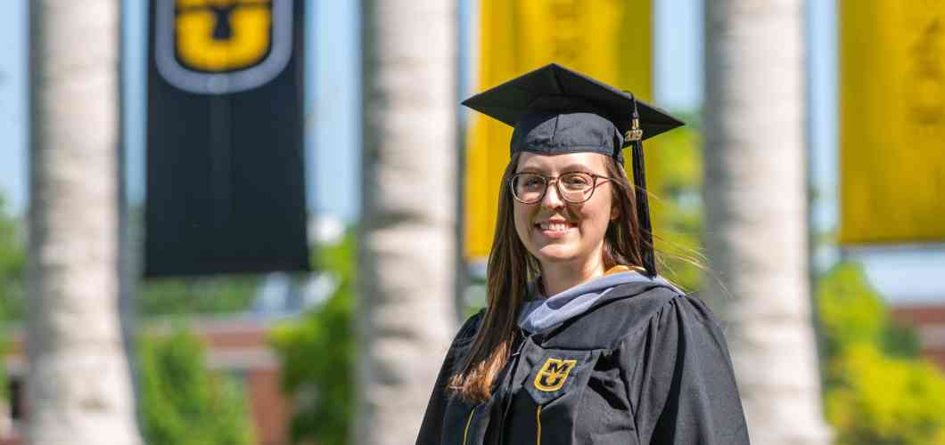 Stephanie Gillam, biomedical sciences MS, wearing a graduation cap and gown in front of Mizzou's columns.