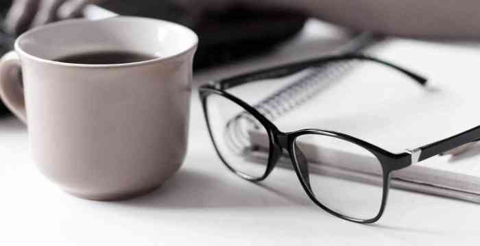 Remote working from home. Freelancer workplace in kitchen with laptop, cup of coffee, spectacles. Concept of distance learning, isolation, female business, shopping online. Close up of woman hands.