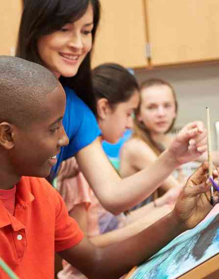 an art teacher, in a classroom of art students, helps one student with painting