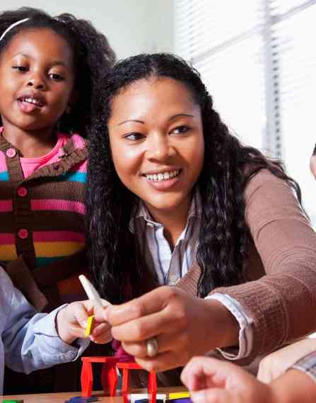 a young black female teacher laughs with group of young engaged students