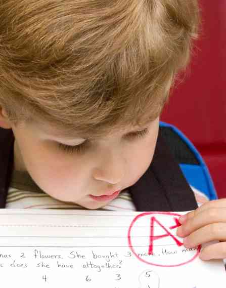 A young child holds a paper with an "A+"