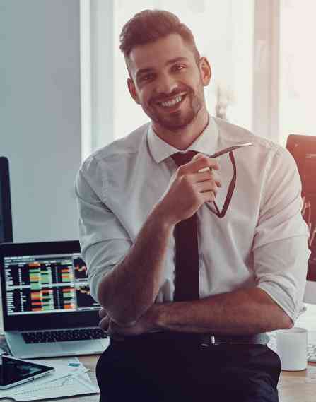 A finance professional sitting on a desk with computer screens behind them.