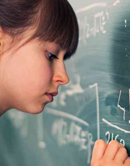a young female student works out a problem on a chalkboard