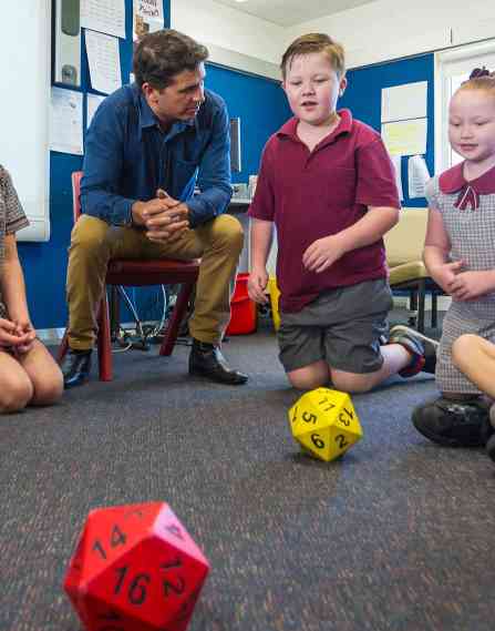 A male teacher playing a dice game with young students