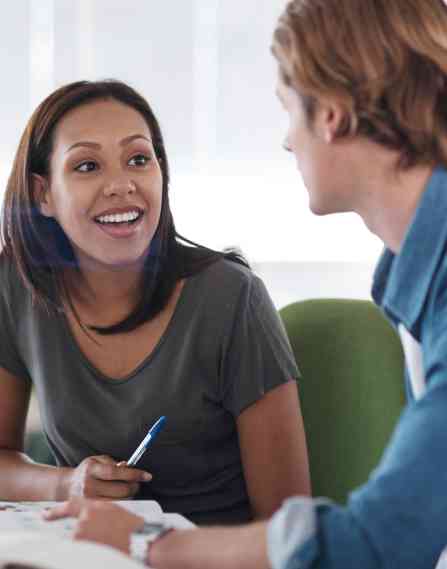 Two people talking at a desk with a laptop.