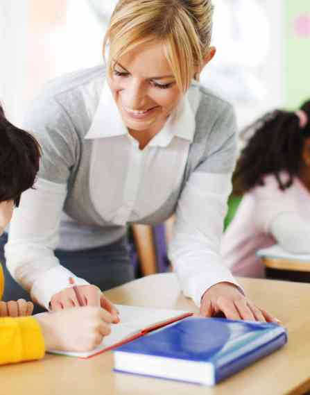 A female teacher smiling at a student sitting at his desk