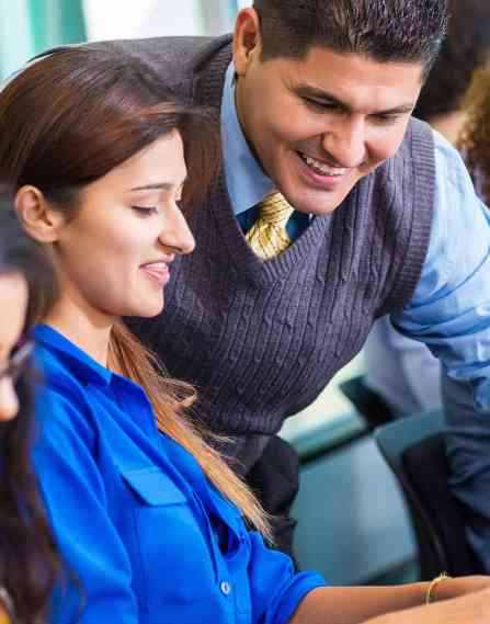 A male teacher leaning over to help a female student on her laptop