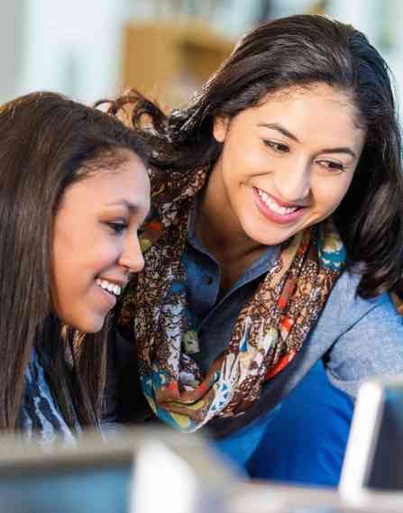 two women looking at a desktop monitor together and smiling