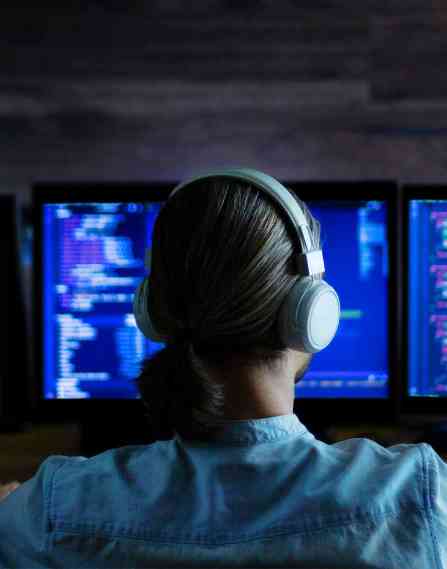 Cybersecurity professional wearing headphones and sitting in front of computer screens.