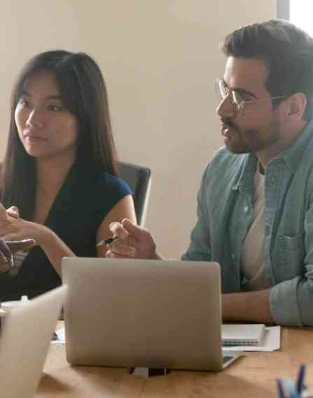 Multiethnic millennial colleagues talk dispute share thoughts on startup project launch at team meeting in office, diverse coworkers brainstorm speak discuss business ideas at briefing together