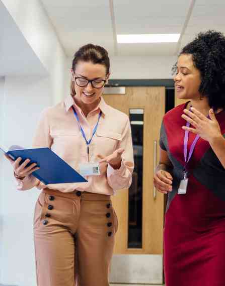 Two female teachers are walking and talking together down the school hall.
