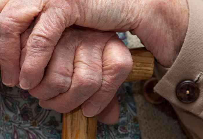 An older adult's hands holding a cane.