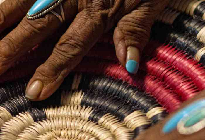 black hands working on a woven multi-color basket 