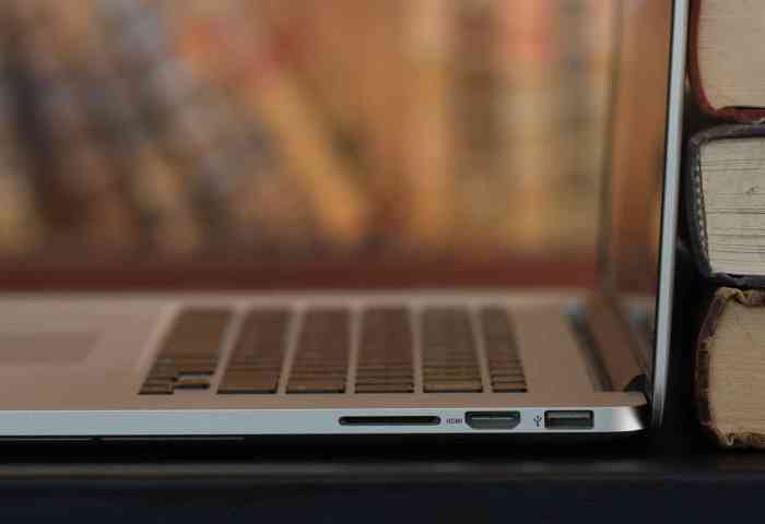 Profile view of a laptop sitting on a desk with books behind the screen.