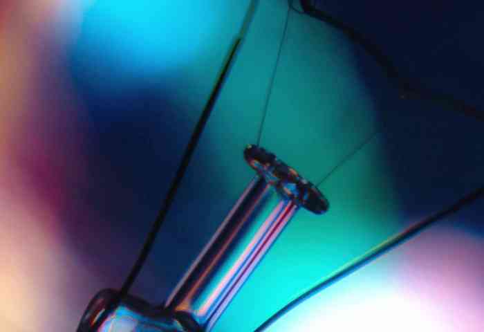 Close up of an incandescent light bulb with a blurry colorful background.