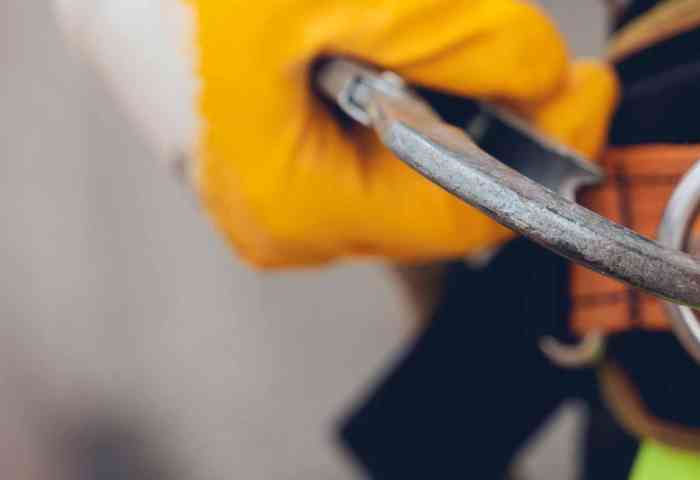 Close up of a workers hands with orange gloves clipping into a safety line.