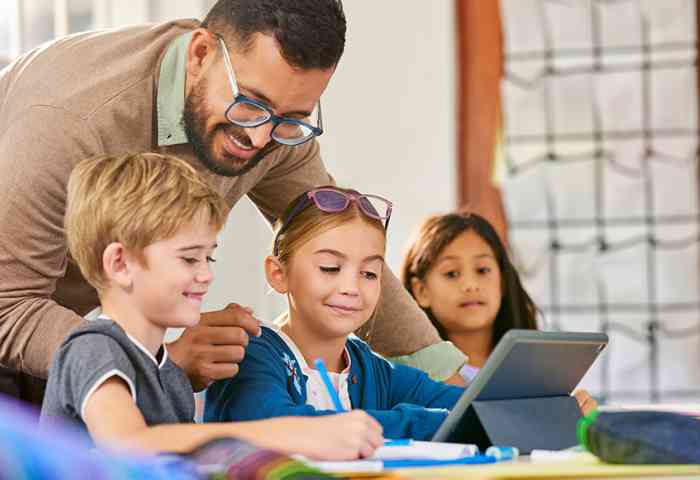 Teacher looking over the shoulders of students to view their assignments.