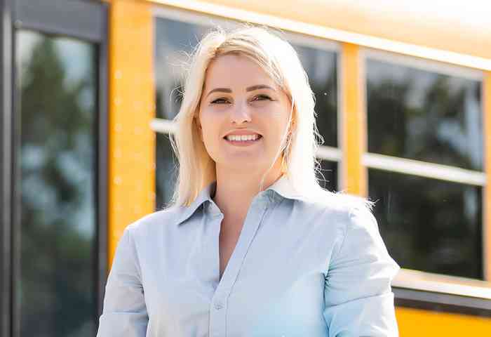 Woman smiling at the camera standing in front of a school bus.