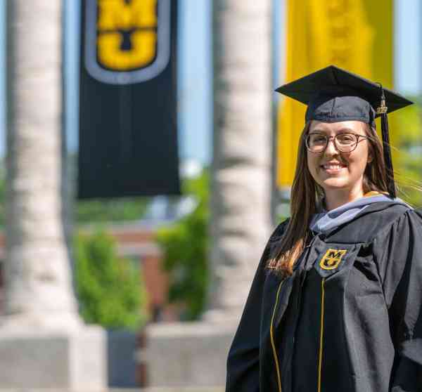 Stephanie Gillam, biomedical sciences MS, wearing a graduation cap and gown in front of Mizzou's columns.
